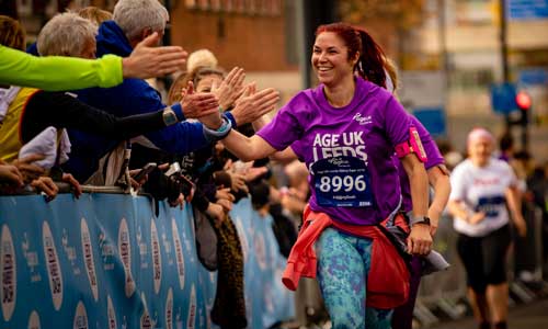 Woman giving high fives to the crowd whilst running in the Age ſֱ Leeds Abbey Dash